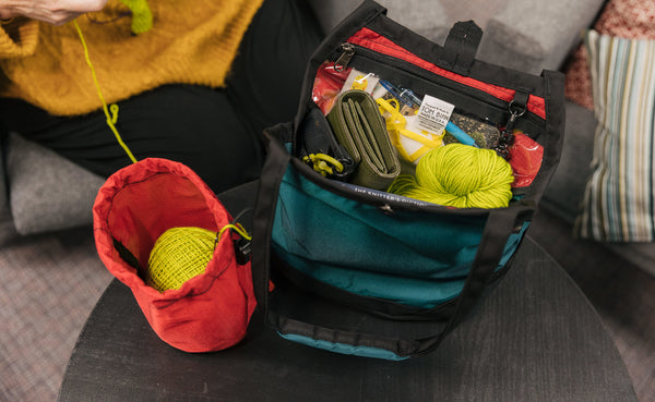 A person knitting out of a Yarn Stuff Sack with a full Little Swift beside it.